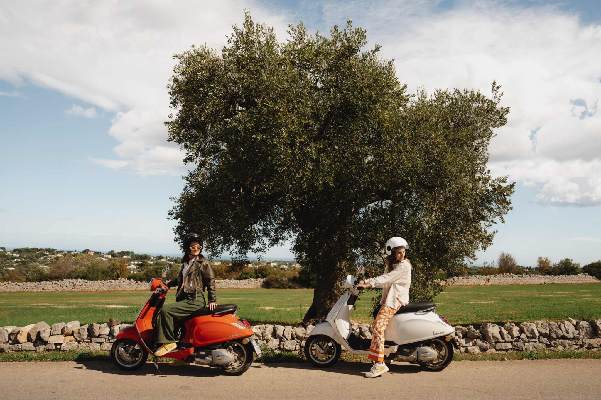 two women on vespas infront of olive tree